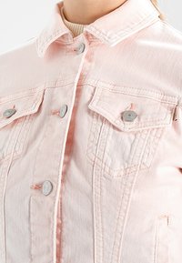 Ljusrosa denimjacka med en klassisk krage, två bröstfickor med silverknappar och subtila sömdetaljer.