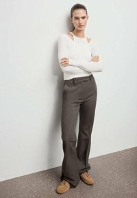 Top bianco a maniche lunghe con dettagli a taglio, abbinato a pantaloni marroni a gamba larga su misura e scarpe color cammello. Design semplice, aderente e texture.