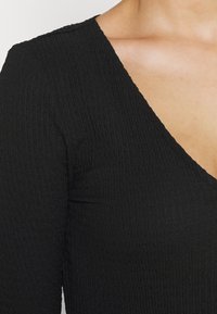 Top nero con una texture a coste, caratterizzato da un profondo scollo a V e maniche corte, che mette in risalto l'elasticità e la morbidezza del tessuto.