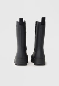 Bottes de pluie en caoutchouc noir avec une finition texturée, dotées d'une fermeture éclair sur le côté et d'une languette à l'arrière pour un enfilage facile.
