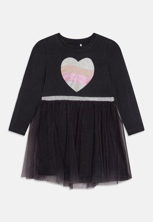 Robe noire à manches longues avec un motif de cœur scintillant. Ceinture argentée et jupe en tulle noir superposée. Matière en coton doux.