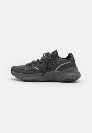 Dunkelgrauer Sportschuh mit dicker, strukturierter Sohle, gestricktem Obermaterial, Schnürverschluss und Markenlogo an der Seite, von der Außenseite gezeigt.
