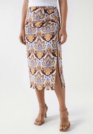 Falda midi de estampado marrón con acentos azules y naranjas, abertura lateral y textura suave. Combinada con tacones altos beige con tiras.