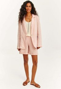 Světle růžový lněný blejzr s odpovídajícími šortkami. Přes krémový pletený top. Hnědé nazouvací sandály. Uvolněný střih s texturovanou tkaninou.