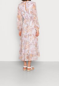 Ljuslila blommig maxiklänning med långa puffärmar, volangsläp och nyckelhålsdetalj i ryggen. Bärs med vita sandaler med remmar.