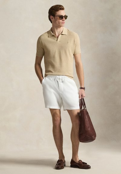 Μπεζ πικέ πόλο πουκάμισο, άσπρο σορτς με κορδόνια, καφέ δερμάτινη τσάντα, σκουρόχρωμα γυαλιά ηλίου και καφέ μοκασίνια· απλό φόντο.