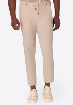 Uomo che indossa pantaloni beige slim fit con tasche frontali e vita con coulisse, abbinati a sneakers casual beige.