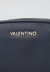 Navy leather handbag featuring a pebbled texture and gold-tone "VALENTINO" logo. Zipper closure along the top. Compact and structured design.