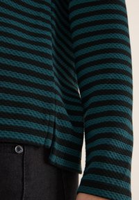 Maglia a maniche lunghe a righe in teal e nero, realizzata in un tessuto testurizzato con righe orizzontali. Presenta una lieve fessura laterale nella parte inferiore.
