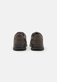 Braune Lederschuhe mit abgerundeter Zehenpartie, strukturiertem Finish und robusten schwarzen Gummisohlen mit einem gemusterten Profil. Dezente Nähdetails.