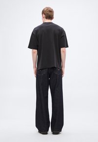 Μαύρο κοντομάνικο t-shirt με άνετη εφαρμογή, συνδυασμένο με σκούρο μπλε τζιν παντελόνι φαρδιάς γραμμής με εμφανείς ραφές και δύο πίσω τσέπες.