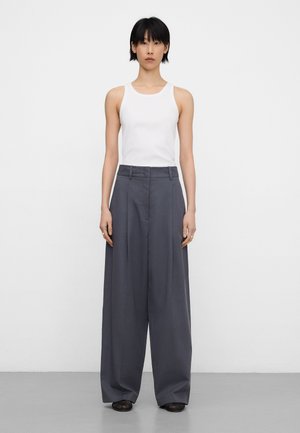 Top bianco senza maniche abbinato a pantaloni grigi a vita alta e gamba larga. Il tessuto appare liscio con un design nitido e linee pulite.