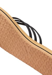 Black strappy sandal with a textured tan rubber sole, featuring a hexagonal grip pattern and a narrow black line along the edge.