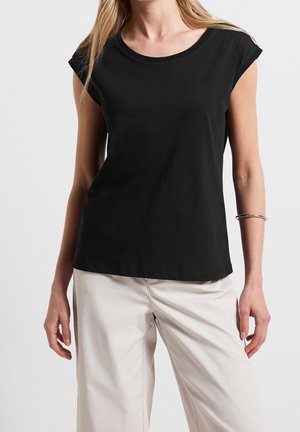 Czarna, bawełniana koszulka z krótkim rękawem, o zaokrąglonym dekolcie, gładkiej teksturze i luźnym kroju, zestawiona z jasnymi spodniami.