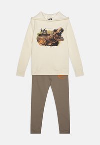 Creme hoodie med dinosaur grafik og helikopterprint; parret med brune leggings med et orange logo. Blødt bomuldsblandingsmateriale.
