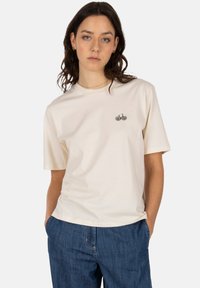 Cream-colored cotton t-shirt with short sleeves, featuring a small embroidered bicycle design on the chest. Textured fabric, casual fit.