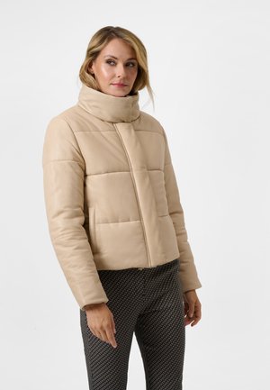 Korte beige pufferjack met een hoge kraag, horizontaal gestikte patronen en zijzakken. Gecombineerd met patroontjesbroek.