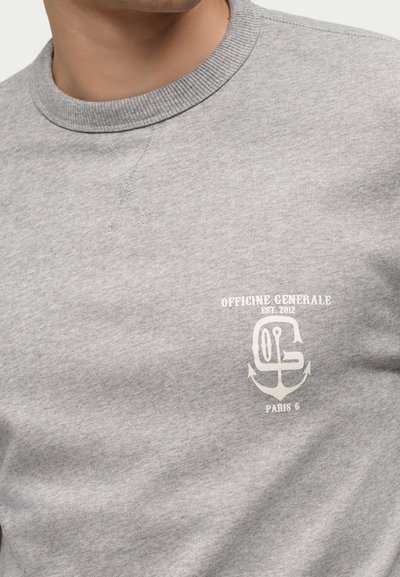 Άνδρας που φορά γκρι φούτερ με λευκό λογότυπο Officine Generale Paris 6 και γραφικό άγκυρας στο στήθος.