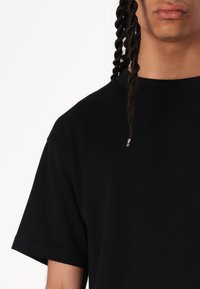 Tricou negru cu mânecă scurtă, fabricat din bumbac. Are un guler rotund și o croială relaxată. Textură netedă, cusături minime vizibile.