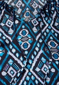 Gemusterter Stoff mit einem blau-weißen geometrischen Design auf schwarzem Hintergrund, mit einer weichen Textur und einem gerafften Kragen. 