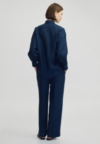 Navyblaue Leinenbluse und passende Hose, die eine lockere Passform, lange Ärmel und Knopfdetails an den Ärmelbündchen der Bluse aufweisen.