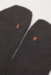 Grå sokker laget av myk stoff med broderte oransje "L" og "R" merker på toppen av hver sokk som angir venstre og høyre.