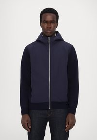 Marinblå huvarjacka med dragkedja fram, kombinerade material; slät kropp med texturerade ribbade muddar och fåll, tvåfärgad design.