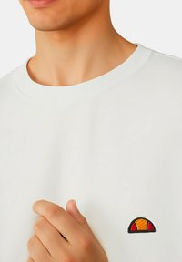 Felpa bianca in cotone con colletto a costine, caratterizzata da un piccolo logo multicolore ricamato sul lato sinistro del petto. Tessuto morbido, design informale.