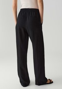 Schwarze weit geschnittene Hose mit elastischem Bund und Gesäßtaschen. Hergestellt aus leichtem Stoff, der eine glatte Textur aufweist.