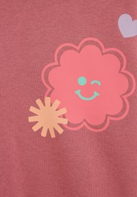 A rózsaszín pamutanyag egy mosolygó virág és nap mintát ábrázol kontrasztos színekben. A virágnak hullámos szegélyei vannak, kis szív díszítéssel.