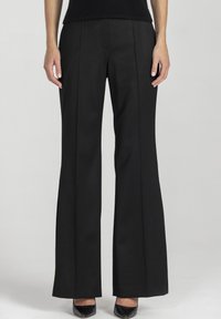 Czarne spodnie dzwony o gładkiej strukturze, z przednimi zakładkami i dopasowanym krojem, zestawione z czarnymi szpiczastymi szpilkami.