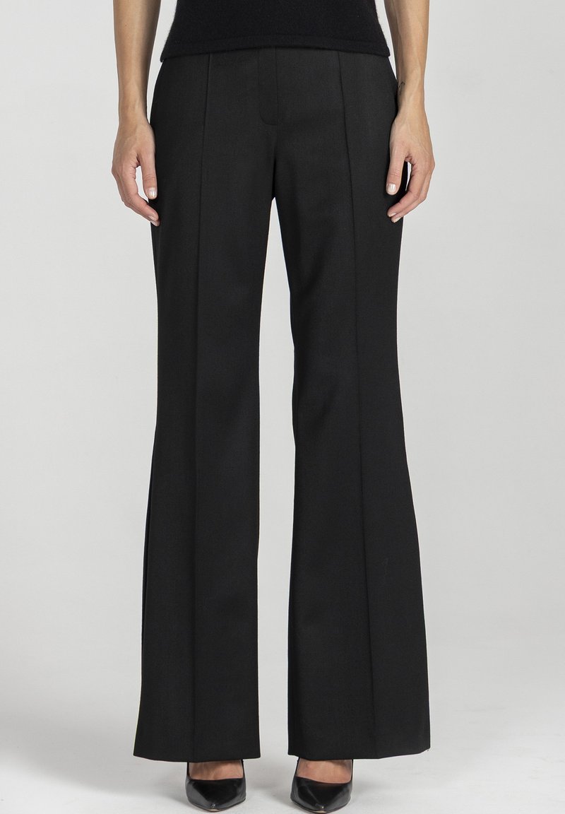 Czarne spodnie dzwony o gładkiej strukturze, z przednimi zakładkami i dopasowanym krojem, zestawione z czarnymi szpiczastymi szpilkami.