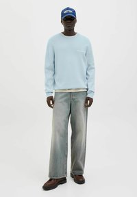 Light blue fleece sweater with ribbed cuffs, paired with faded wide-leg jeans. Brown boots and a blue cap complete the outfit.
