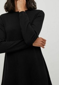 Svart långärmad klänning i mjukt tyg, med rundad hals och avslappnad passform, med subtil textur och en enkel design.