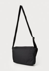 Sac messager noir de forme rectangulaire. Fabriqué en tissu durable, il dispose d'une longue bandoulière adjustable et d'un design épuré et minimaliste.