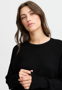 Schwarzer Strickpullover mit runden Ausschnitt, gerippten Bündchen und lockerer Passform. Die Textur ist weich und dezent gemustert.