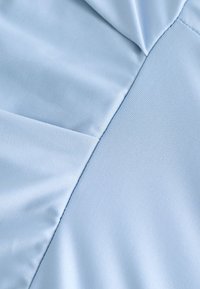 Primer plano de tela azul clara con secciones lisas y ligeramente texturizadas unidas por costuras visibles.