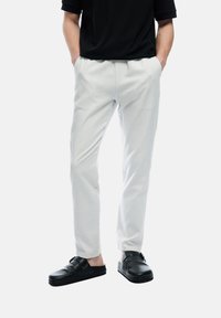 Lichtgrijze broek met een taps toelopend ontwerp en gestructureerde stof. Gepaard met zwarte instappers met gesps Accent.