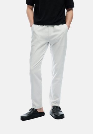 Lichtgrijze broek met een taps toelopend ontwerp en gestructureerde stof. Gepaard met zwarte instappers met gesps Accent.