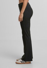 Černé proužkované zvonové kalhoty z texturované látky, s vysokým pasem a v kombinaci se světlými teniskami.