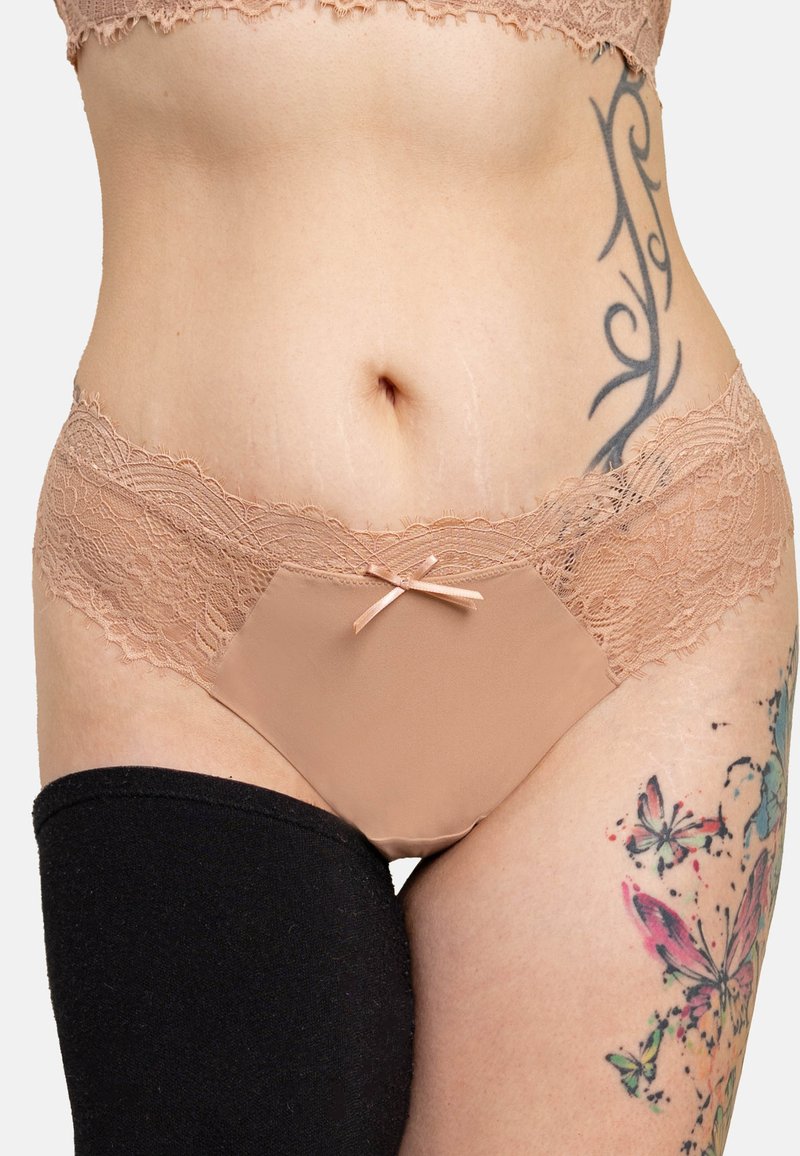 Nudefarbener Spitzen-Slip mit Satin-Schleifenakzent, mit transparentem Spitzenbund und einer glatten Stoffvorderseite. Schwarzer Stoff am linken Oberschenkel.