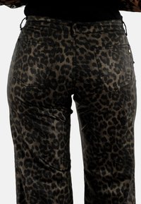 Pantalones de estampado de leopardo en negro y marrón, con una textura suave, cinco bolsillos y detalles de costura sutiles en la cintura y el dobladillo.