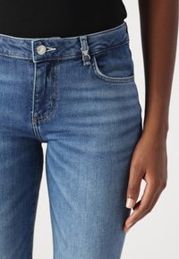 Jeans in denim azzurro chiaro con vita alta, design a cinque tasche, chiusura con bottone in metallo e dettagli di cucitura delicati lungo le cuciture.