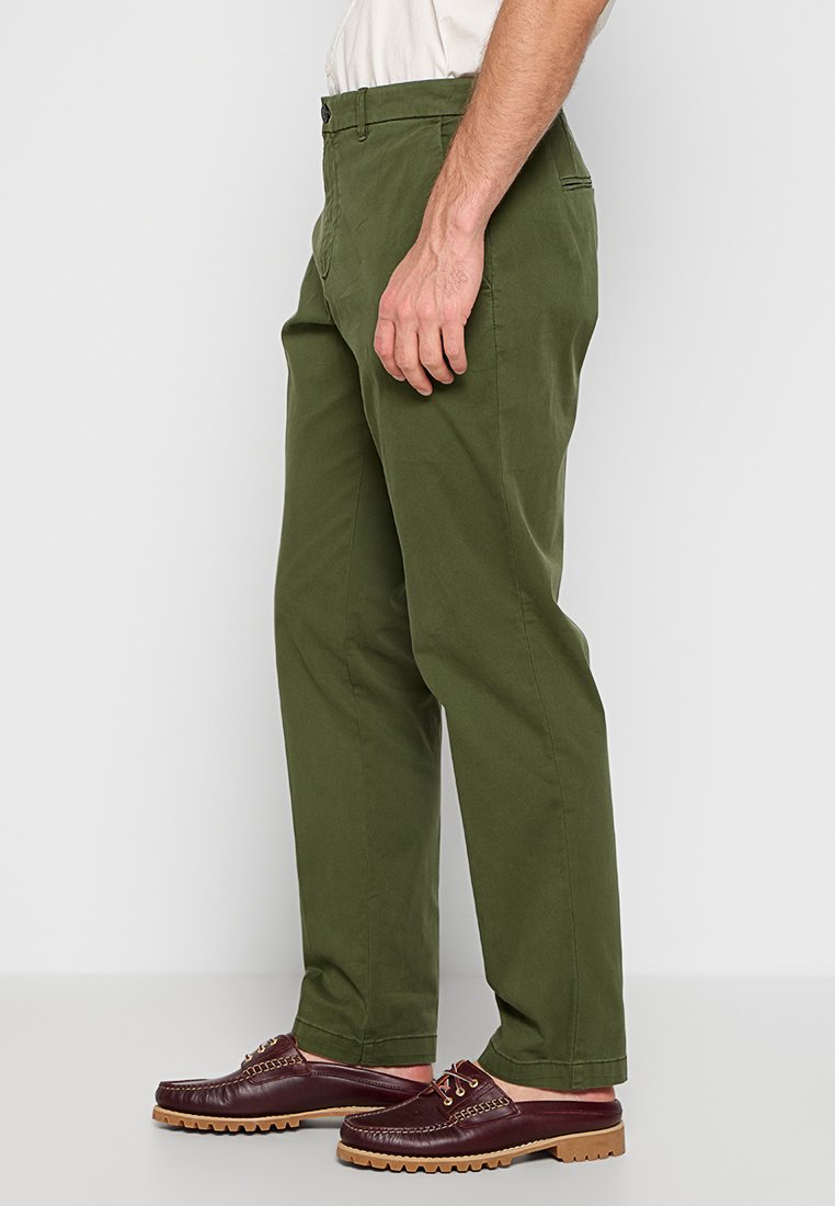 Pantaloni di cotone verdi con design a gamba dritta, dotati di tasche laterali e passanti per la cintura, abbinati a scarpe slip-on marroni scure.