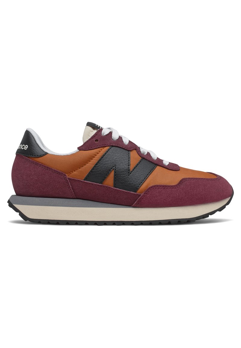 Zapatilla deportiva en color marrón y naranja con un logo N negro, parte superior de ante y nailon, cierre de cordones y entresuela gris, con una suela de goma texturizada.