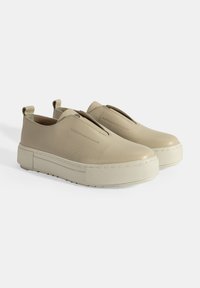 Beige leren instapschoenen met een gestructureerde afwerking, voorzien van een dikke witte plateauzool en elastische zijpanelen voor gemakkelijk aan- en uittrekken.