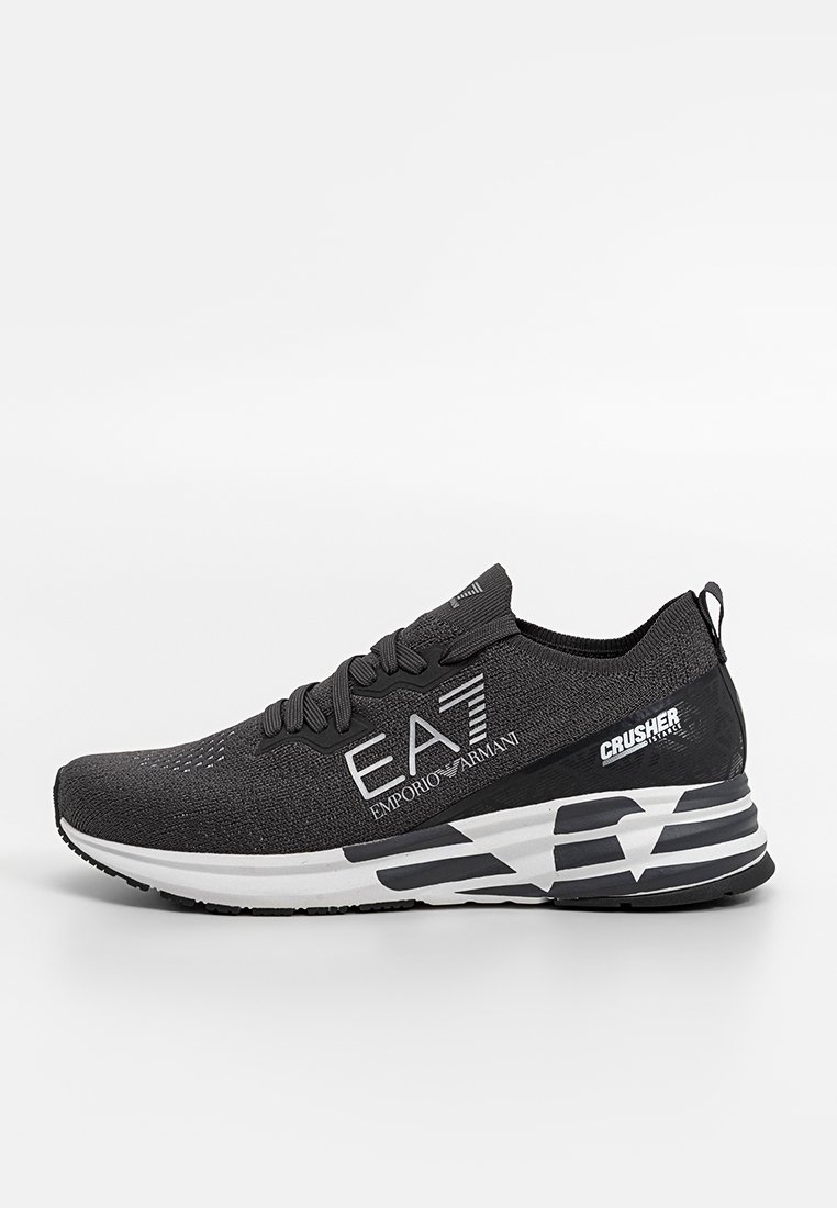 Schwarzer Sportschuh mit einem Mesh-Obermaterial, das ein Strickdesign aufweist, bedruckte Logos und eine klobige weiße und schwarze Sohle mit geometrischem Muster.