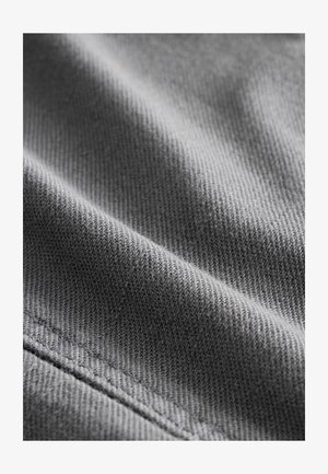 Tessuto grigio con una superficie strutturata e una delicata trama diagonale, con dettagli di cucitura lungo un bordo.