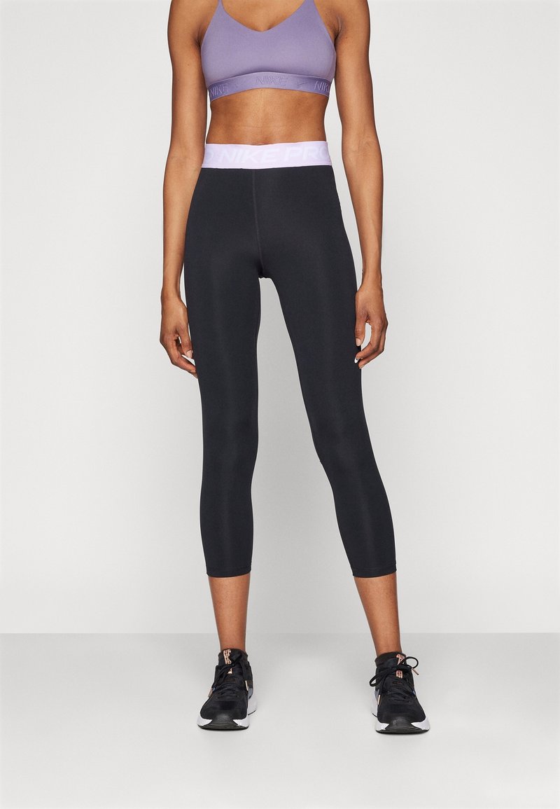 Zwarte capri leggings met een roze Nike Pro tailleband, gecombineerd met een lila sportbeha. De stof lijkt glad en rekbaar.