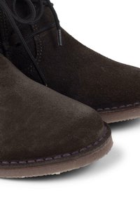 Botas de tobillo de ante marrón con puntera redondeada, diseño con cordones y un contraste de costura púrpura a lo largo de la suela con un acabado texturizado mínimo.